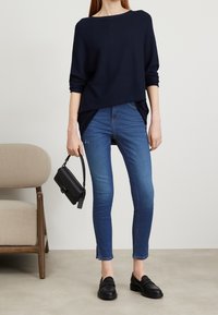 Maglione a maglia navy, vestibilità ampia, con maniche arrotolate. Jeans skinny azzurri, lunghezza alla caviglia. Borsa nera con tracolla piccola e chiusura. Mocassini neri.