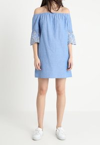 Blue off-the-shoulder dress with lace-trimmed bell sleeves, made of lightweight fabric; worn with white fringe sneakers.