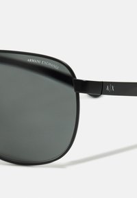 Ochelari de soare negri cu lentile rectangulare și finisaj mat. Prezintă un logo argintiu "Armani Exchange" și un accent "A/X" pe braț.