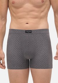 Torso masculino luciendo un ajustado bóxer gris con pequeño patrón de diamantes rojos y etiqueta de Ysabel Mora en el centro de la cinturilla.
