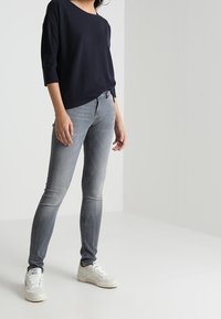 Laivansinisellä neulepaitalla, jossa on kolmannes hihat, yhdistetty vaaleanharmaisiin skinny-farkkuihin ja valkoisiin tennareihin. Yksinkertainen, rento asu.