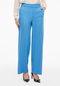 Modré široké kalhoty s texturovanou tkaninou, mají rovný střih, poutka na opasek a boční kapsy. Kombinované s černými vysokými podpatky.