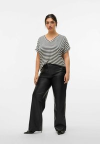 Top a righe con scollatura a V in bianco e nero abbinato a pantaloni a palazzo in ecopelle nera a vita alta. Tessuto liscio con maniche arrotolate.
