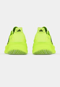 Een paar neon groene sportschoenen gezien vanuit de achterkant, met een zwart Adidas-logo op de hielriemen en gestructureerde rubberen zolen.