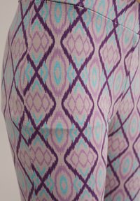 Violeta un tirkīza rakstainas legingi ar dimanta motīvu uz gaišas fona, izgatavoti no mīkstas, strukturētas auduma.