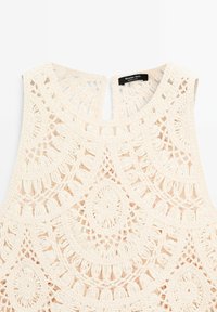 Haut sans manches en crochet crème avec des motifs circulaires et floraux complexes, encolure ronde et petite ouverture en forme de goutte à l'arrière.