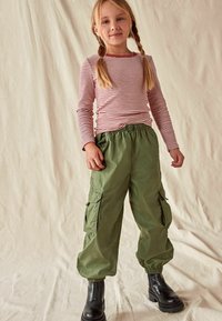 Gestreiftes Langarmoberteil in Rot und Weiß, kombiniert mit grünen Cargo-Hosen mit Seitentaschen, elastischen Bündchen und schwarzen Knöchelschuhen.