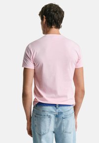 Lichtroze katoenen t-shirt met een ronde hals en korte mouwen, gedragen met blauwe jeans met een gevlochten riem in een zichtbare tailleband.