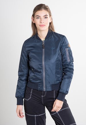 Marineblauwe bomberjas met ritssluiting aan de voorkant, geribbelde manchetten en tailleband. Voorzien van een zak met klep op de mouw en een logo op de borst. Heeft een gladde textuur.