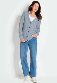Grijs-blauwe gebreide cardigan met een v-hals, knopen aan de voorkant en geribde manchetten, gecombineerd met lichtblauwe wijde jeans en witte sneakers.