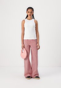 Weißes geripptes Tanktop, pinke und weiße gestreifte weit geschnittene Hose und eine runde pinke Tasche. Das Outfit hat eine lässige, entspannte Passform.