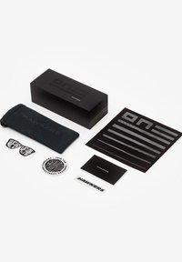 Ambalajul de tip cutie neagră conține un săculeț gri pentru ochelari de soare, autocolante și un mic booklet. Toate articolele prezintă un design minimalist și culori monocrome.