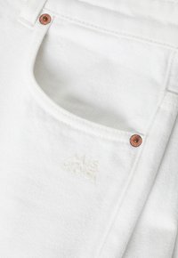 Tessuto di denim bianco con finitura testurizzata, dotato di una tasca frontale, accessori in rame e un ricamo del marchio in bianco.