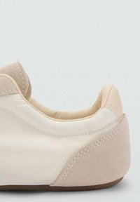 Chaussure de sport beige avec une tige en satin lisse et un talon en daim. Présente un col rembourré et une semelle en caoutchouc flexible. Les coutures sont visibles.