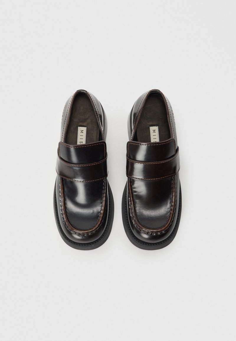 Mocassins en cuir noir avec une finition brillante, présentant une large sangle sur le coup de pied, des coutures contrastées et une forme de pointe arrondie.