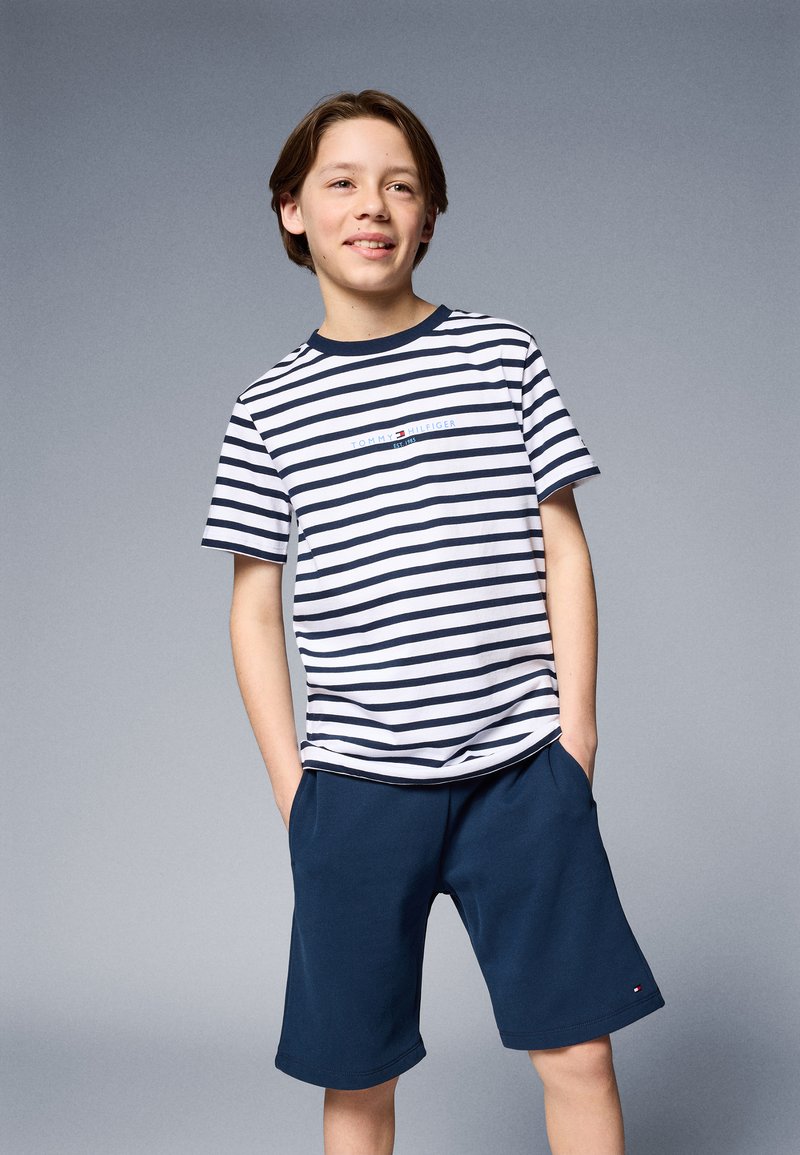 T-shirt à manches courtes rayé en bleu marine et blanc, avec un logo sur la poitrine, associé à un short bleu foncé, tous deux en tissu en coton.