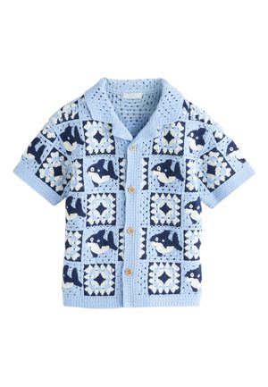 Lyseblå hæklede cardigan med korte ærmer, knapper foran og vekslende mønstre af hvaler og geometriske firkanter i marineblå og hvid.