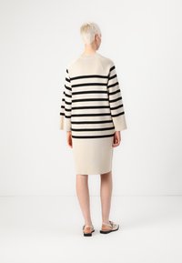Stripet kjole i beige og svart, med rund halslinje, lange ermer, og en rett fasong som faller akkurat over knærne.