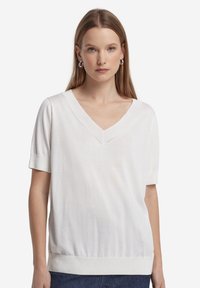T-shirt bianca a maniche corte con scollo a V, polsini a costine e vita aderente. Realizzata in tessuto morbido e leggero con una trama liscia.