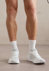 Białe buty sportowe z teksturowaną siateczką u góry i gumową podeszwą, w parze z białymi skarpetkami z prążkami. Buty mają prosty, nowoczesny design.