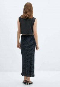 Schwarze Jeansweste in Cropped-Länge über einem blauen Karottenrock bis zum Knöchel mit einer weichen, fließenden Textur. Schwarze Sandalen mit Riemchen runden das Outfit ab.