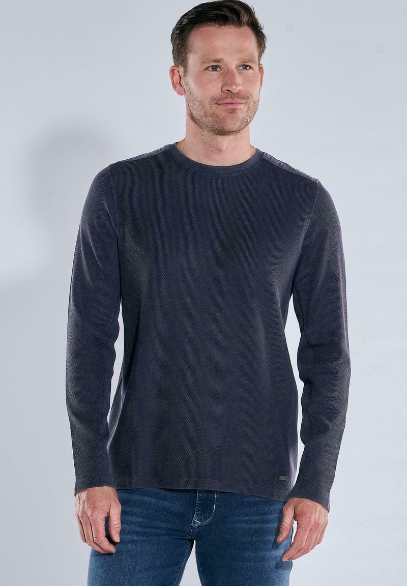 Dunkelgraues Langarmshirt aus strukturiertem Stoff mit Rundhalsausschnitt und dezenten Schulterdetails, kombiniert mit blauen Jeans.