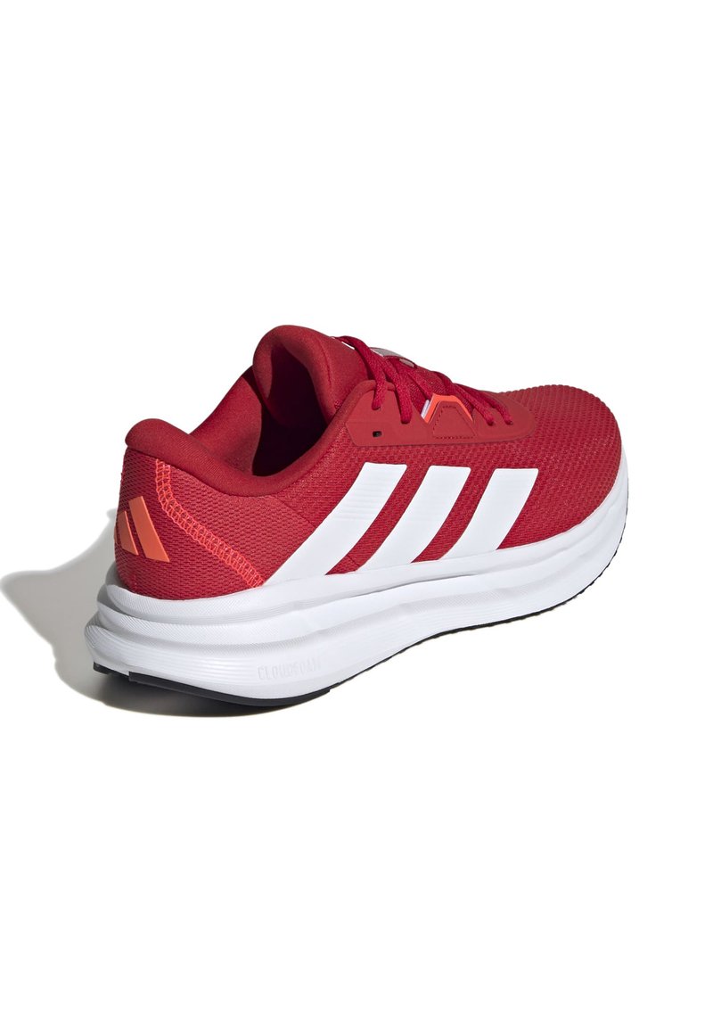 Zapatilla deportiva roja con parte superior de malla texturizada. Presenta marcas de tres rayas blancas, un cuello acolchado y una suela media blanca gruesa con suela exterior negra.