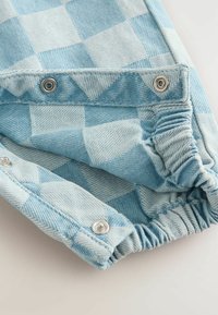 Lys blåternet denimstof med synlige trykknapper og samling af elastik ved kanten. Har et struktureret, vævet mønster.