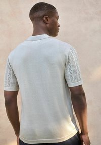 Camisa polo gris claro con mangas cortas y textura de punto con patrón. Cuello clásico y diseño ajustado con una silueta limpia.