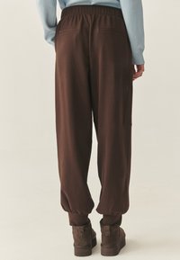 Brązowe zwężane spodnie z elastycznym pasem, z dwoma tylnymi kieszeniami i mankietami przy kostkach, w połączeniu z brązowymi botkami.