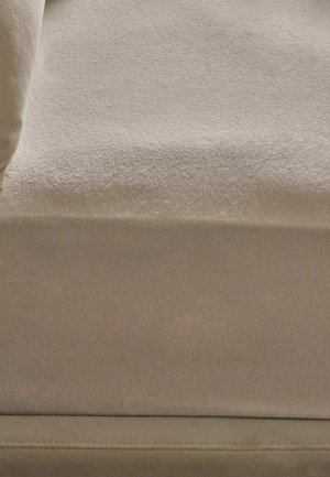 Nahaufnahme einer hellbeigen Stoffoberfläche mit weicher Textur und einer sichtbaren Naht nahe dem unteren Rand.