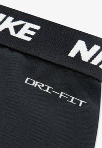 Mustat urheilusukat, joissa on teksturoitu kuvio, näkyvällä valkoisella "NIKE"-logolla varren kohdalla ja hopeinen "DRI-FIT"-merkintä.