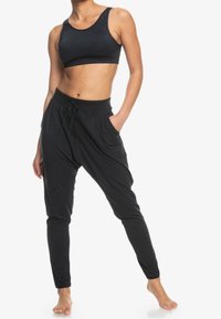 Zwarte atletische crop top en aangesloten broek, gemaakt van zachte stof, met een elastische tailleband met trekkoord en zijzakken. Gladde textuur en aansluitend design.