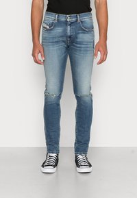 Blå denimjeans med en urtvättad look, slitna knäområden och smal passform. Kombinerade med svarta hög-ankel sneakers och en svart skjorta.