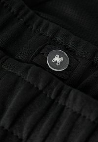 Bouton rond transparent en plastique cousu sur un tissu noir avec des bandes élastiques froncées, montrant une texture détaillée et des coutures.