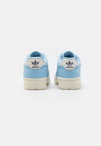 Modré kožené tenisky s bílým patním poutkem, se třemi černými pruhy a logem Adidas na zadní straně. Gumová podrážka, nízký střih.