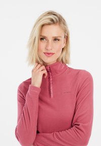 Pullover in pile rosa con collo alto, zip a metà e logo ricamato. Texture morbida e maniche lunghe. Vestibilità casual.