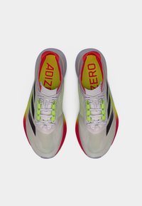 Hvide løbesko i mesh med klare neon grønne og røde accenter, der har et let design, polstret sål og flade snørebånd.