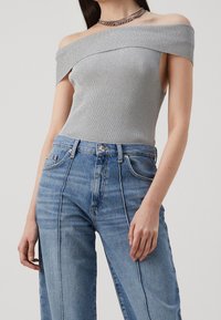 Top gris de canalé con hombros al aire combinado con jeans de tiro alto en azul claro que cuentan con costuras verticales y un corte relajado.