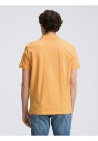Kortärmad polo skjorta i livlig orange bomull. Har en klassisk krage och enkel design, tillsammans med blå denimjeans.