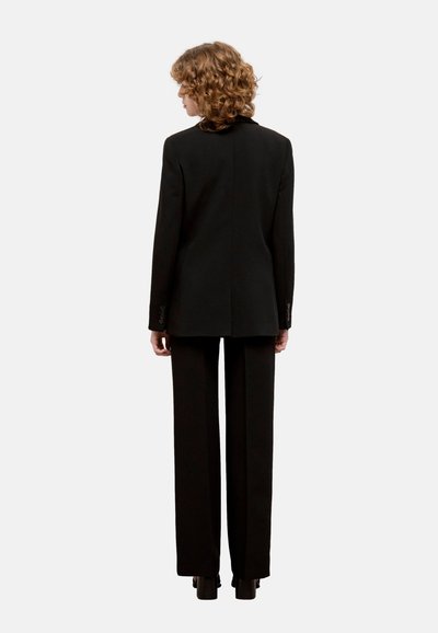 Completo nero su misura con giacca aderente e pantaloni a gamba larga. Tessuto liscio, design minimalista, linee pulite e senza motivi visibili.