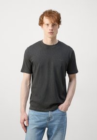 Tricou scurt cu mânecă scurtă, de culoare gri închis, dintr-un material moale; guler rotund; prezintă un logo subtil pe piept; asortat cu blugi de culoare albastru deschis.