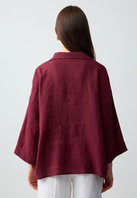 Bordowa lniana koszula o luźnym kroju, szerokich rękawach i klasycznym kołnierzyku. Teksturowana tkanina o gładkim wykończeniu, widoczne szwy z tyłu.