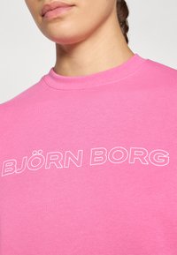 En rosa crew neck sweatshirt laget av bomull, med teksten "BJÖRN BORG" i hvitt over brystet, med en glatt og ensfarget tekstur.