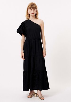 Robe maxi noire à une épaule avec une manche bouffante texturée. Possède une jupe à volants avec des détails brodés à l'ourlet. Le modèle porte des talons dorés.
