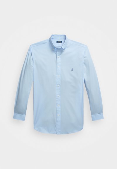 Gaiši zila garām piedurknēm pogājama krekls, izgatavots no gludas auduma, ar pogojamu apkakli un mazu izšūtu logotipu kreisajā krūtī.