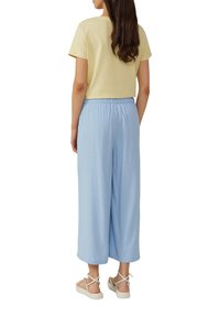 Korte gele t-shirt, lichtblauwe wijde broek, elastische tailleband en beige sandalen met kruisbandjes.