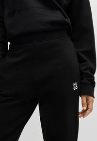 Zwarte sweatpants met geribde boorden, voorzien van een klein wit "HUGO" logo aan de zijkant. Het materiaal heeft een soepele, zachte textuur.