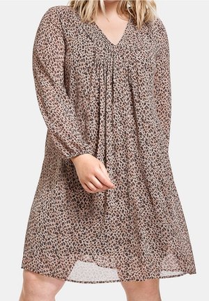 Vrouw die een losse, lange mouwen, knie-lange jurk draagt met een roze en zwarte luipaardprint en een V-hals.