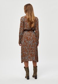 Brun kjole med blåt abstrakt mønster, lange ærmer, taljebånd og en svajende nederdel. Sammen med olivenfarvede ankelstøvler med block heels.